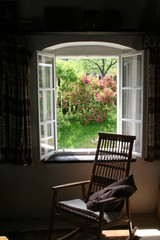 Rocking chair in front of open window with blooming bush outside