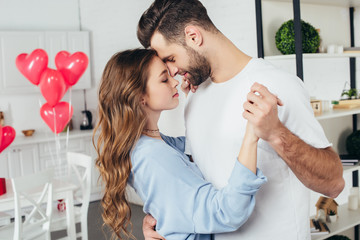selective focus of beautiful happy couple dancing on st valentine day with heart-shaped balloons on background