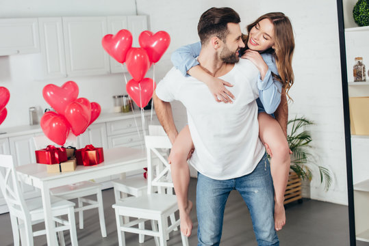 happy couple piggybacking at home in room with st valentine day decoration