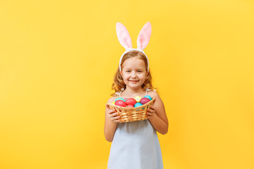 Obraz na płótnie Canvas Cute little child girl with bunny ears holding basket of Easter eggs on a colored background.