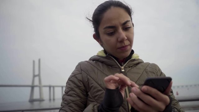 Thoughtful hindu woman using smartphone outdoor. Beautiful brunette holding smartphone during overcast weather. Technology concept