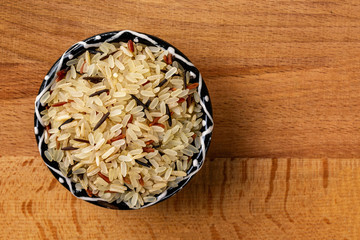 Obraz na płótnie Canvas Top view bowl of raw white, brown and black rice mix at wooden table background arranged at left side.