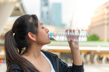 Teenage girls are drinking water from plastic bottles, because they are tiredness from exercise with blurred soft of tall building in the city background, to drink concept.