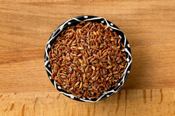 Top view bowl of red rice at wooden board background arranged at centre.