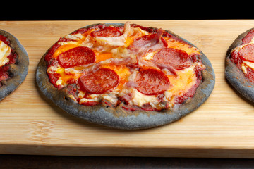 Creative pizza on black dough, wooden plank.