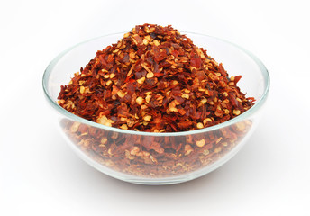 Crushed red hot pepper pile / sun dried chili flakes and seeds in glass bowl isolated on white background