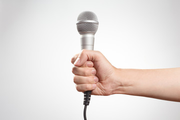 Male hand holding a microphone on gray background