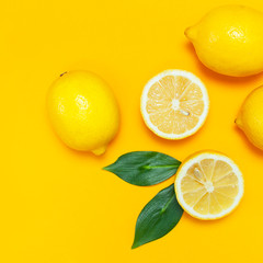 Ripe juicy lemons and green leaves on bright yellow background. Lemon fruit, citrus minimal concept, vitamin C. Creative summer food minimalistic background. Flat lay, top view, copy space.