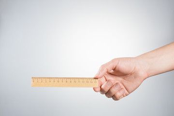 Hand holding wooden ruler on gray background