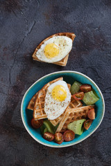 Breakfast including waffles, fried eggs and vegetables, above view on a grey cracked stone background