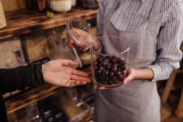 Shop assistant holding glass jar with healthy chocolate balls in organic store.