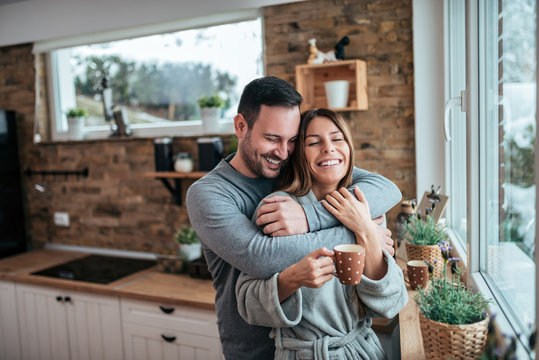 Beautiful Couple Hugging At The Kitchen In The Winter Morning.