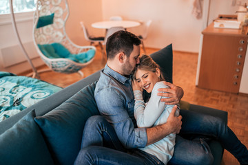 Young couple cuddling on the couch at home.