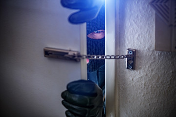 burglar with torch opens door of appartment - obrazy, fototapety, plakaty