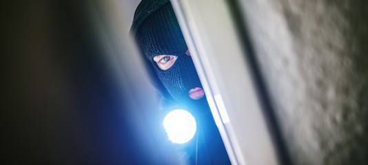 burglar with torch opens door of appartment - obrazy, fototapety, plakaty