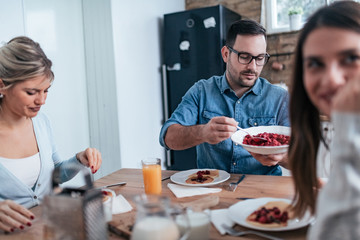 Friends eating homemade pancakes with berries at home.