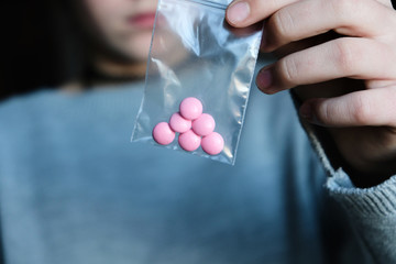 Woman holding in her hand pink pills in a little plastic bag zipper. Drugs, medecine, narcotik