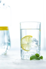 glass cup and a carafe of water, ice, mint and lemon on a white table