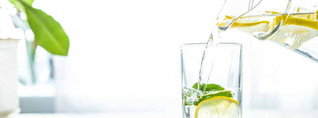 Pouring a glass of water with lemon, ice and mint on a white table