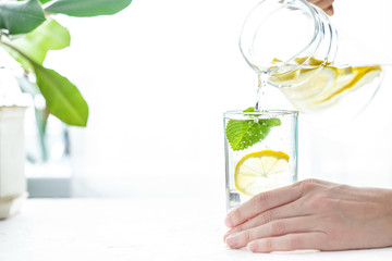 Pouring a glass of water with lemon, ice and mint on a white table