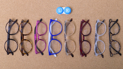 Fototapeta na wymiar Different eyeglass frames on cork board and small container with contact lenses