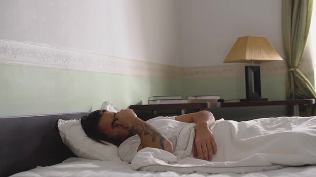 Sleepy guy in pajamas unwillingly gets out of bed and leaves the bedroom