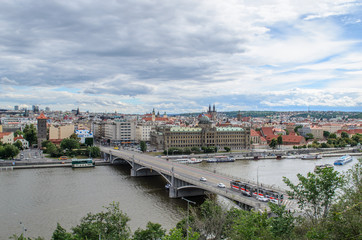 Fototapeta na wymiar View of the Ministry of Industry of the Czech Republic. Beautiful view of Prague, one of the new bridges. Tram and cars drive over the bridge over the Vltava river. Ship sailing along the river. On th