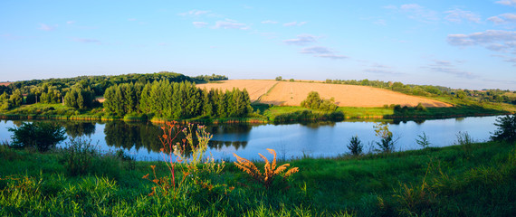 Sunny panorama with river flowing between the golden wheat fields and green meadows.