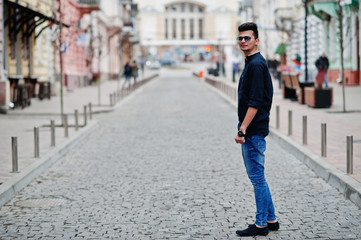 Stylish indian model man in casual clothes, black shirt and sunglasses posed outdoor at street of India.