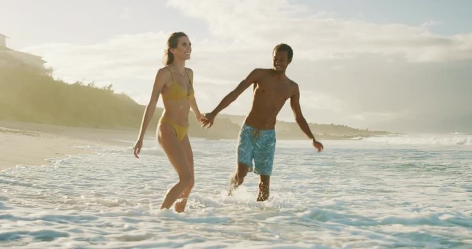 Adorable mixed race couple walking and splashing on the shore at sunset