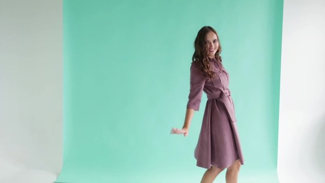 Young funny girl in a beautiful pink dress dancing and laughing. A girl with blond hair is dancing on a grey background. A girl is dancing in her dress. The girl is spinning and having fun
