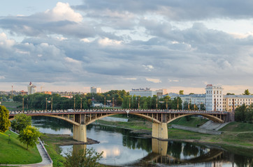 Fototapeta na wymiar Vitebsk. The bridge over the Vitba River, which flows into the Western Dvina. Republic of Belarus. Beautiful view of the city. City landscape. Sunset, textured sky, a lot of clouds, small river in sum