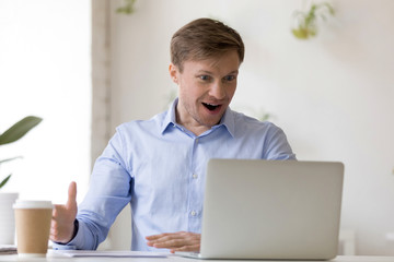 Pleasantly surprised, shocked businessman looking at laptop screen, man feeling excited about online win, watching funny video in social network at workplace, enjoying, receiving good news, offer