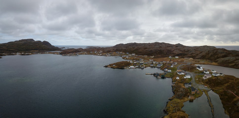 Aerial panoramic view of a small town on a rocky Atlantic Ocean Coast during a cloudy day. Taken in Goose Cove East, near St. Anthony, Newfoundland, Canada.