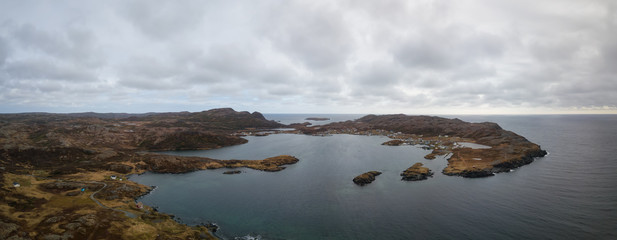 Aerial panoramic view of a small town on a rocky Atlantic Ocean Coast during a cloudy day. Taken in Goose Cove East, near St. Anthony, Newfoundland, Canada.