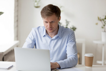 Serious focused businessman looking at laptop screen, doing computer work, concentrated man writing...