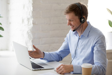 Smiling businessman in headphones looking at laptop screen, watching good webinar, consulting client, distance learning languages, making notes, happy man participating online conference - obrazy, fototapety, plakaty