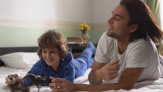 Two brothers lying on the bed play with toys. Older and younger brothers having fun together.