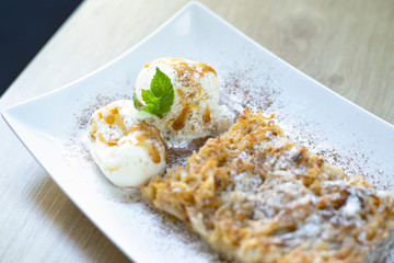 Delicious fresh dessert with mint leaves, sprinkled with powdered sugar, is on the table, in a white square plate.