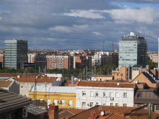 diversidad urbana de edificios, casitas bajas, tejaditos rojos de teja y detrás rascacielos de hormigón y cristal con fondo nublado de ciudad y cielo con nubes
