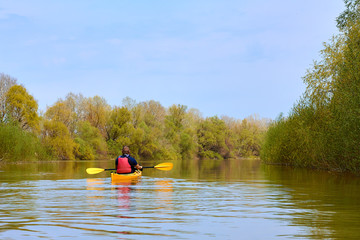 Spring kayaking. Concept for adventure, travel, action, lifestyle. Rear view of kayaker man paddle yellow kayak on Danube river.