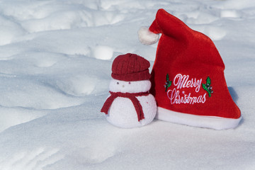 Christmas red hat and a lovely snowmen toy on the white snow, holiday celebration concept.