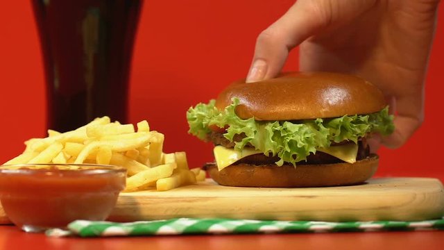 Lady taking burger from fastfood combo, french fries with sauce on wooden plate