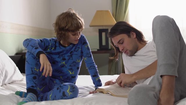 Two brothers lie down in bed, older brother read for small brother a book and high five