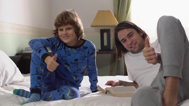 Two brothers lie down in bed, older brother read for small brother a book and they show like to camera. Thumbs up.