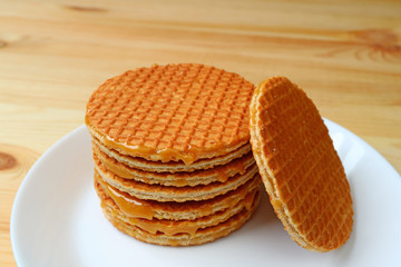 Stack of delectable Stroopwafel or caramel filled Dutch waffle served on white plate on wooden table