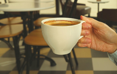 Man's Hand Holding White Cup of Hot Coffee with Blurry French Style Cafe in Background
