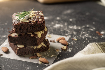 Homemade dark chocolate brownies topping with almond slices stacked on dark plate with copy space....