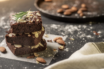 Homemade dark chocolate brownies topping with almond slices stacked on dark plate with copy space. Delicious bitter sweet and fudge. Brownie is one type of chocolate cake.