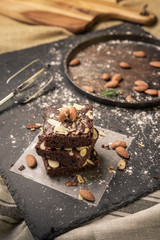 Homemade dark chocolate brownies topping with almond slices stacked on dark plate with copy space. Delicious bitter sweet and fudge. Brownie is one type of chocolate cake.